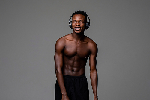 Shirtless fit happy young African man wearing headphones and smiling in light gray isolated studio background