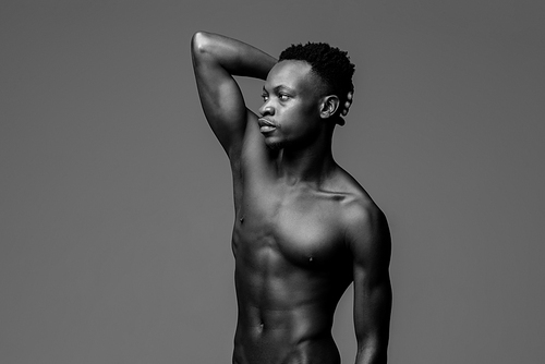 Handsome shirtless muscular African man posing with one arm up, black and white studio portrait