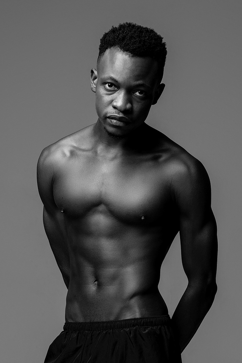 Handsome shirtless muscular African man lookig at camera, black and white studio shot