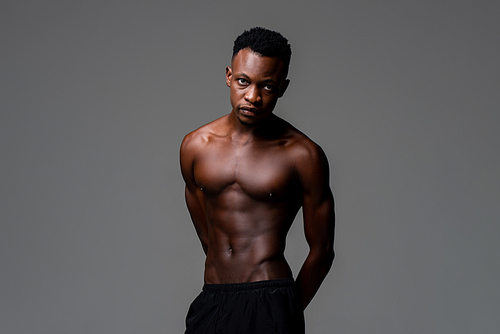 Studio shot of handsome shirtless lean fit African man lookig at camera in isolated gray background