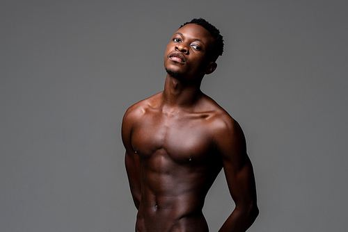 Waist up studio portrait of shirtless young lean fit African man in isolated light gray background