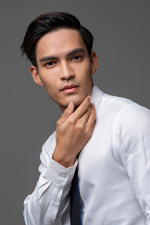 Portrait of smart handsome Asian man in corporate wear touching face in light gray isolated studio background