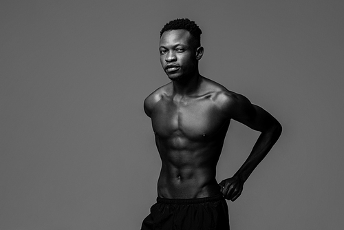 Monochrome studio shot portrait of shirtless fit young handsome African man in isolated studio background