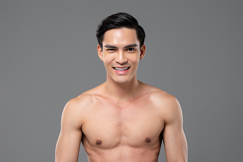 Shirtless handsome cheerful Asian man smiling on isolated gray background for beauty and skin care concept