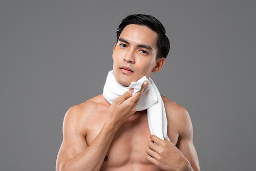 Portrait of shirtless handsome Asian man wiping his face with towel on isolated gray background for beauty and skin care concept