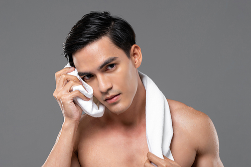 Young handsome shirtless Southeast Asian man wiping his face with towel in isolated studio gray background