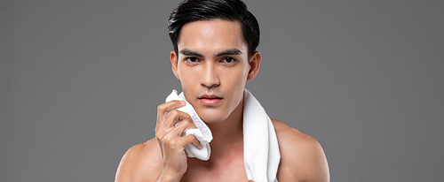 Young handsome shirtless Southeast Asian man wiping his face with towel in isolated studio gray banner background