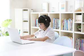 무선 헤드폰을 끼고 노트북으로 온라인 수업을 하는 어린 학생