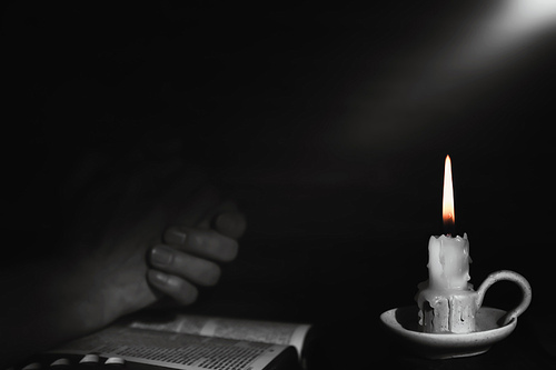 거룩한 성경책과 기도하는 사람 손 그리고 타오르는 촛불 배경과 밝은 빛줄기
