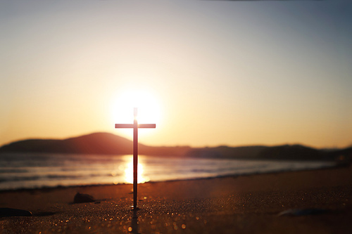 바닷가 붉은 노을과 강한 빛이 반사되는 모래 해변 그리고 예수 그리스도의 거룩한 십자가