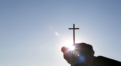 밝게 빛나는 태양과 두 손으로 붙잡은 예수그리스도의 죽음과 부활을 상징하는 거룩한 십자가 배경
