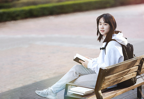 공원 벤치에 앉아 가방을 메고 책을 읽으며 공부하는 고등 학생과 대학생 컨셉