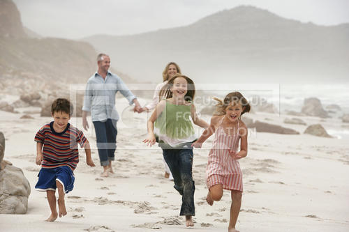 Happy children running on beach with parents walking in background