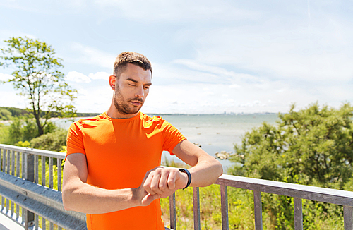 fitness, sport, people and healthy lifestyle concept - young man with smart wristwatch at summer seaside