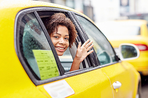 business trip, transportation, travel, gesture and people concept - young smiling african american woman driving in taxi and waving hand at city street