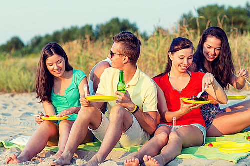 friendship, happiness, summer vacation, holidays and people concept - group of smiling friends having picnic on beach
