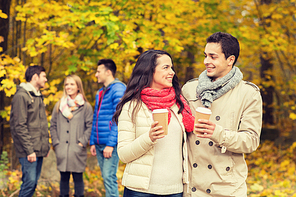 love, relationship, season, friendship and people concept - group of smiling men and women walking with paper coffee cups in autumn park