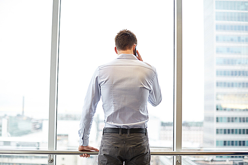 business, technology and people concept - businessman calling on smartphone and looking out office window