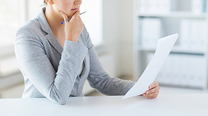business, finance and people concept - close up of woman reading papers or tax report at office