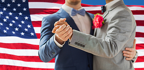 people, homosexuality, same-sex marriage and love concept - close up of happy male gay couple holding hands and dancing on wedding over american flag background