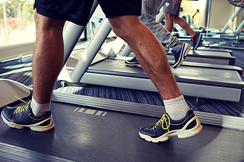 sport, fitness, lifestyle, technology and people concept - close up of men legs walking on treadmills in gym