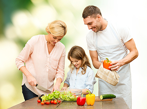 vegetarian food, culinary, happiness and people concept - happy family cooking vegetable salad for dinner over green natural background