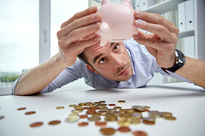 business, people, finances, crisis and money saving concept - businessman shaking piggy bank and getting coins at office
