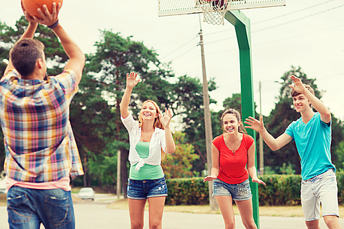 summer vacation, holidays, games and friendship concept - group of smiling teenagers playing basketball outdoors