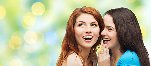 friendship, secrecy and people concept - two smiling girls or young women whispering gossip over green lights background