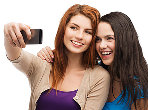 technology, friendship and people concept - two smiling teenagers taking picture with smartphone camera