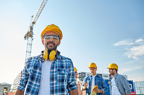 business, building, teamwork and people concept - group of smiling builders in hardhats at construction site