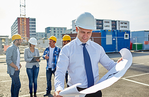 construction, architecture, business, teamwork and people concept - male architect with blueprint over group of builders on construction site