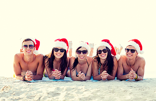 friendship, happiness, summer vacation, holidays and people concept - group of friends in santa helper hats on beach