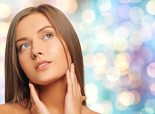 beauty, people and health concept - beautiful young woman touching her neck over blue holidays lights background