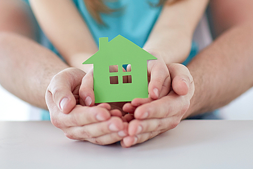 people, charity, family, real estate and home concept - close up of man and girl holding green paper house cutout in cupped hands