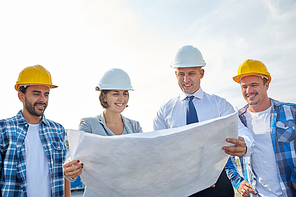 business, building, teamwork and people concept - group of builders and architects in hardhats with blueprint on construction site