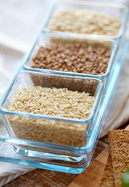 food, agriculture, cereals and healthy eating concept - close up of buckwheat, oatmeal and rice grain on wooden table
