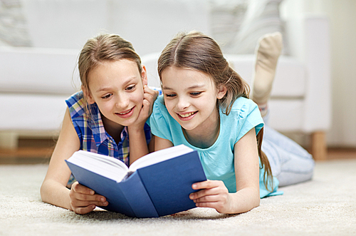 people, children, friends, literature and friendship concept - two happy girls lying on floor and reading book at home