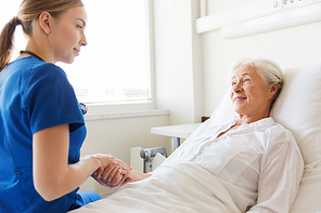 medicine, age, support, health care and people concept - doctor or nurse visiting and cheering senior woman lying in bed at hospital ward