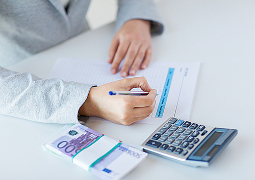 business, finance, tax and people concept - close up of woman hands counting euro money with calculator and tax report form