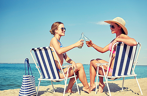 summer vacation, travel and people concept - happy women drinking beer and sunbathing in lounges on beach