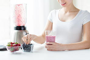 healthy eating, cooking, vegetarian food, dieting and people concept - close up of woman with blender and berries preparing milk shake at home