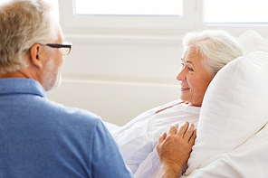 medicine, age, support, health care and people concept - happy senior man visiting and cheering his woman lying in bed at hospital ward