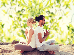 fitness, sport, meditation and lifestyle concept - smiling couple making yoga exercises sitting outdoors