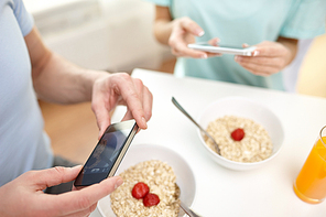 food, eating, people, technology and healthy food concept - close up of couple having breakfast and taking picture with smartphones at home