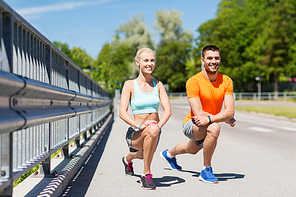 fitness, sport, training and lifestyle concept - smiling couple stretching leg outdoors