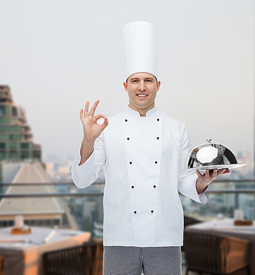cooking, profession, gesture and people concept - happy male chef cook holding cloche and showing ok sign over city restaurant lounge background