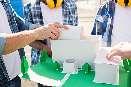 building, construction, teamwork and people concept - close up of builders hands with paper house model or layout outdoors