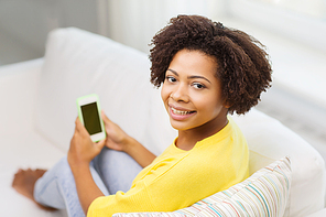 people, technology and leisure concept - happy african american young woman sitting on sofa with smartphone at home