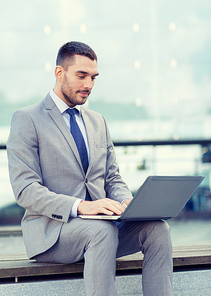 business, education, technology and people concept - businessman working with laptop computer on city street